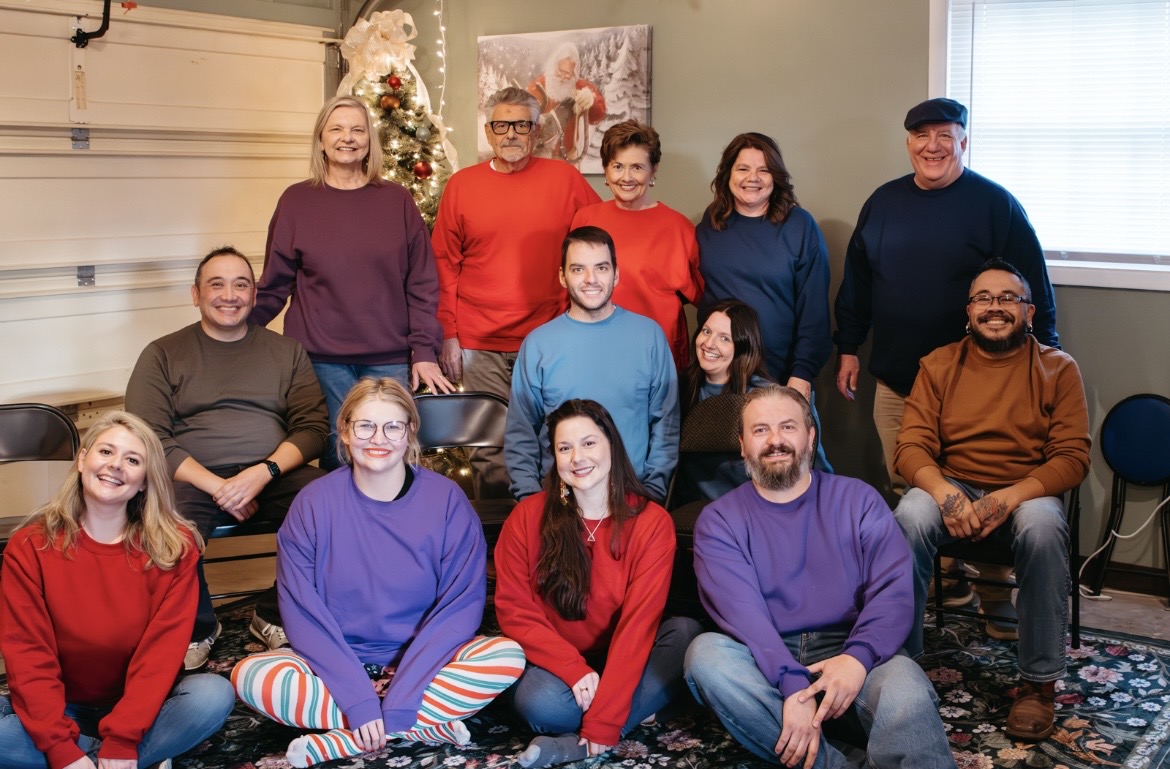 A large multigenerational family in colorful sweaters poses together in front of a Christmas tree, recreating their 1993 family photo